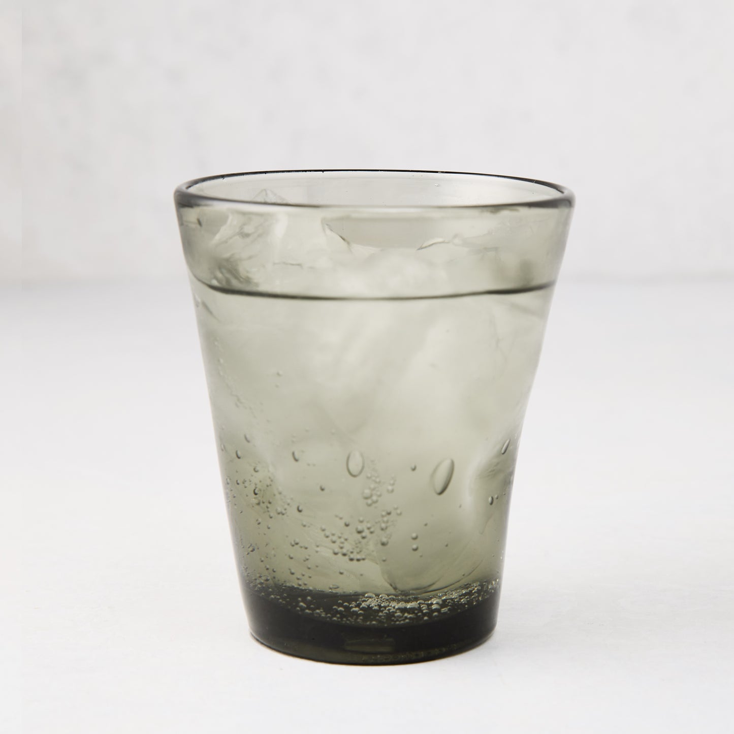 Grey Henri mouth-blown glass, 8 oz, filled with ice and a bubbly drink.