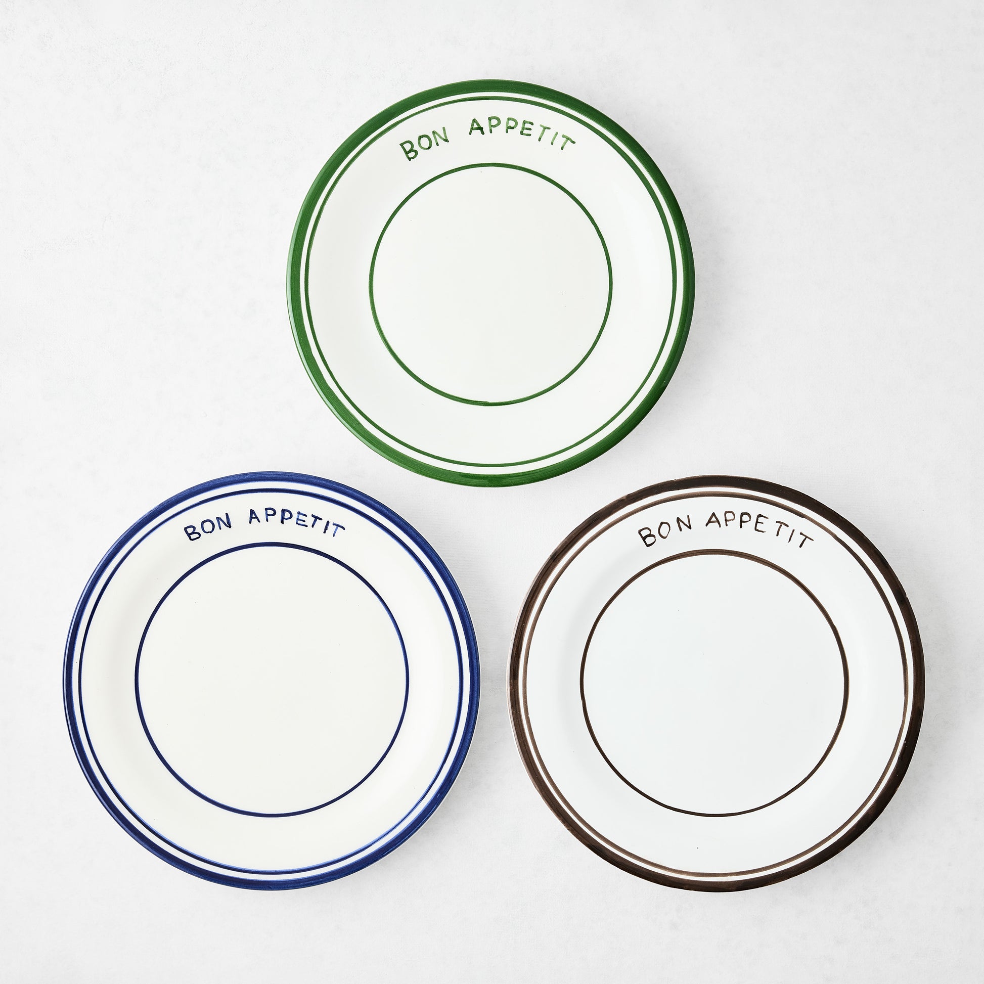 Three ceramic "Bon Appetit" salad plates: green, navy, and chocolate brown, with hand-painted lines.