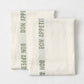 Set of two folded, off-white 100% linen French tea towels with green "Bon Appetit" text and striped detailing.
