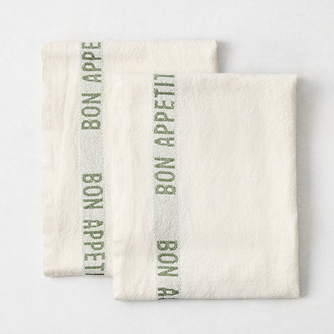 Set of two folded, off-white 100% linen French tea towels with green "Bon Appetit" text and striped detailing.