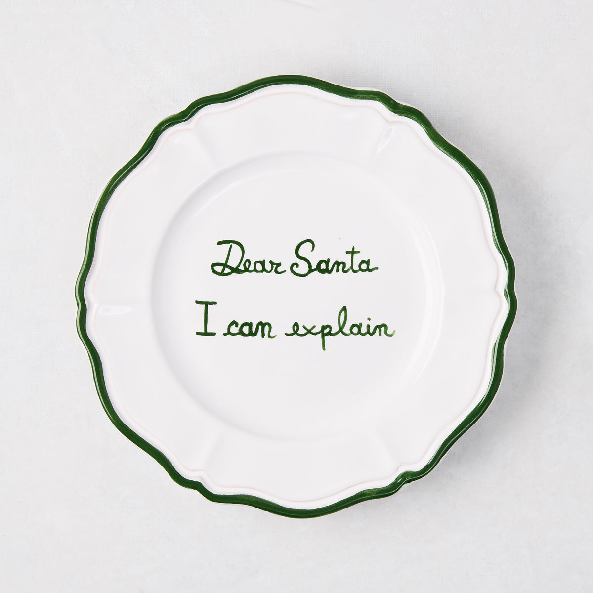 7-inch white ceramic appetizer plate with green hand-painted text reading Dear Santa I can explain and a scalloped green rim.