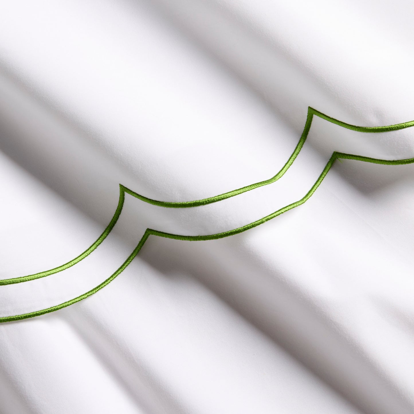 White organic cotton percale sheet with green double scallop stitch embroidery.