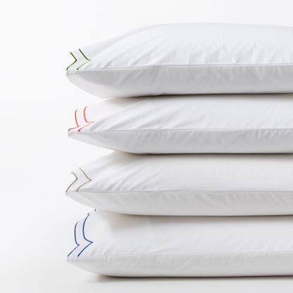 Stack of four white organic cotton percale pillow shams with double scallop stitch embroidery in green, red, tan, and blue.