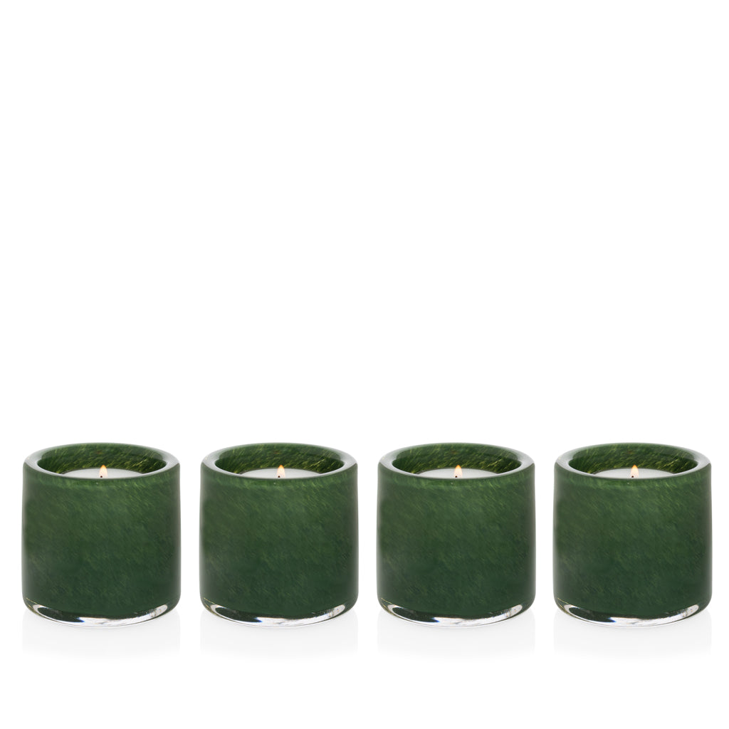 Four mouth-blown, hand-formed green votive glass candle holders with lit candles.