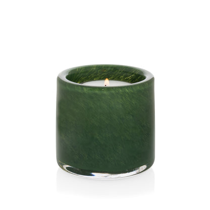 Mouth-blown, hand-formed green votive glass candle holder with a lit candle, reflecting on a white surface.