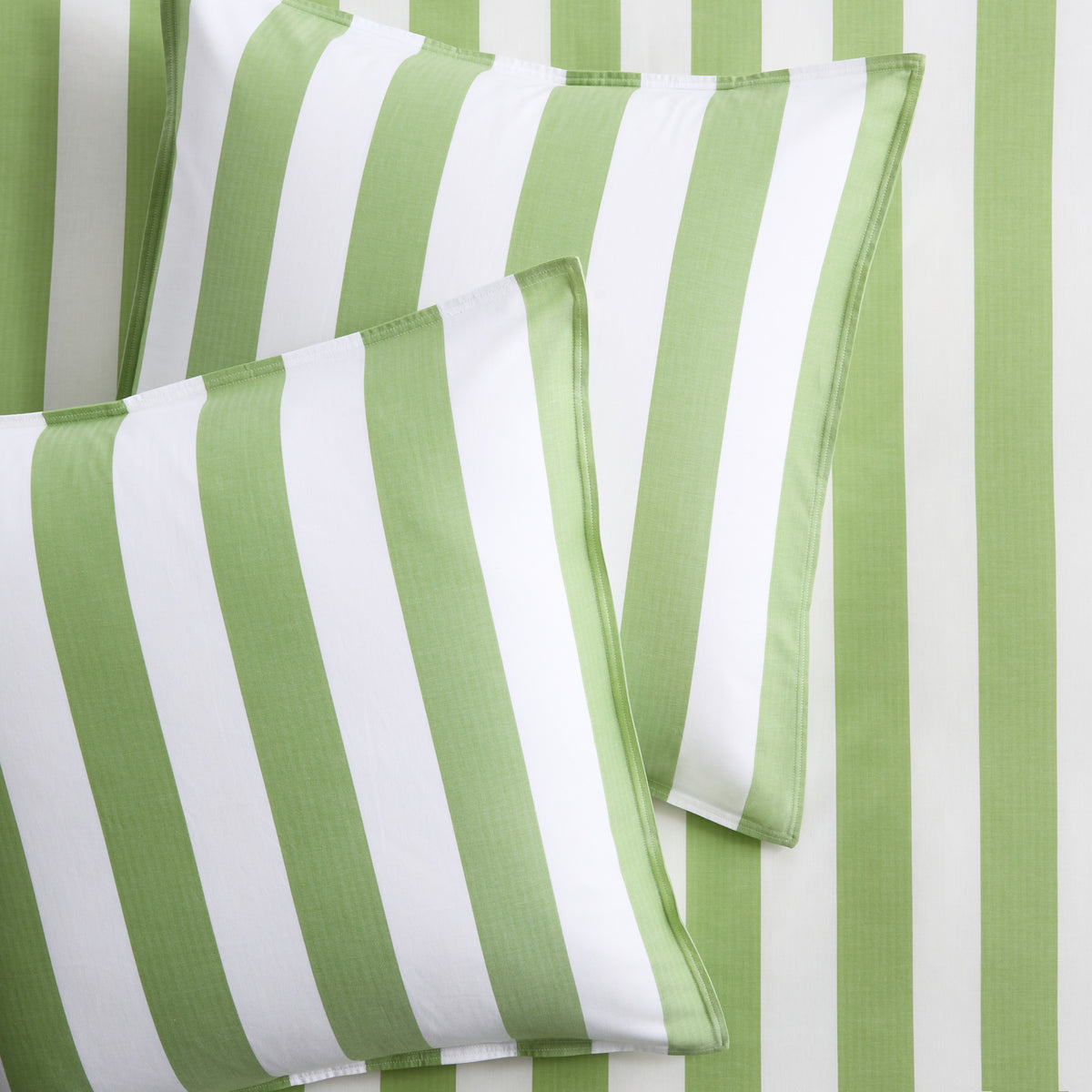 Set of two green and white wide-striped herringbone Euro shams on matching striped bedding.