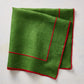 Green linen napkin with red embroidered border detail, folded on a light textured surface.