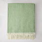 Green Italian herringbone throw blanket, folded, with cream fringe.
