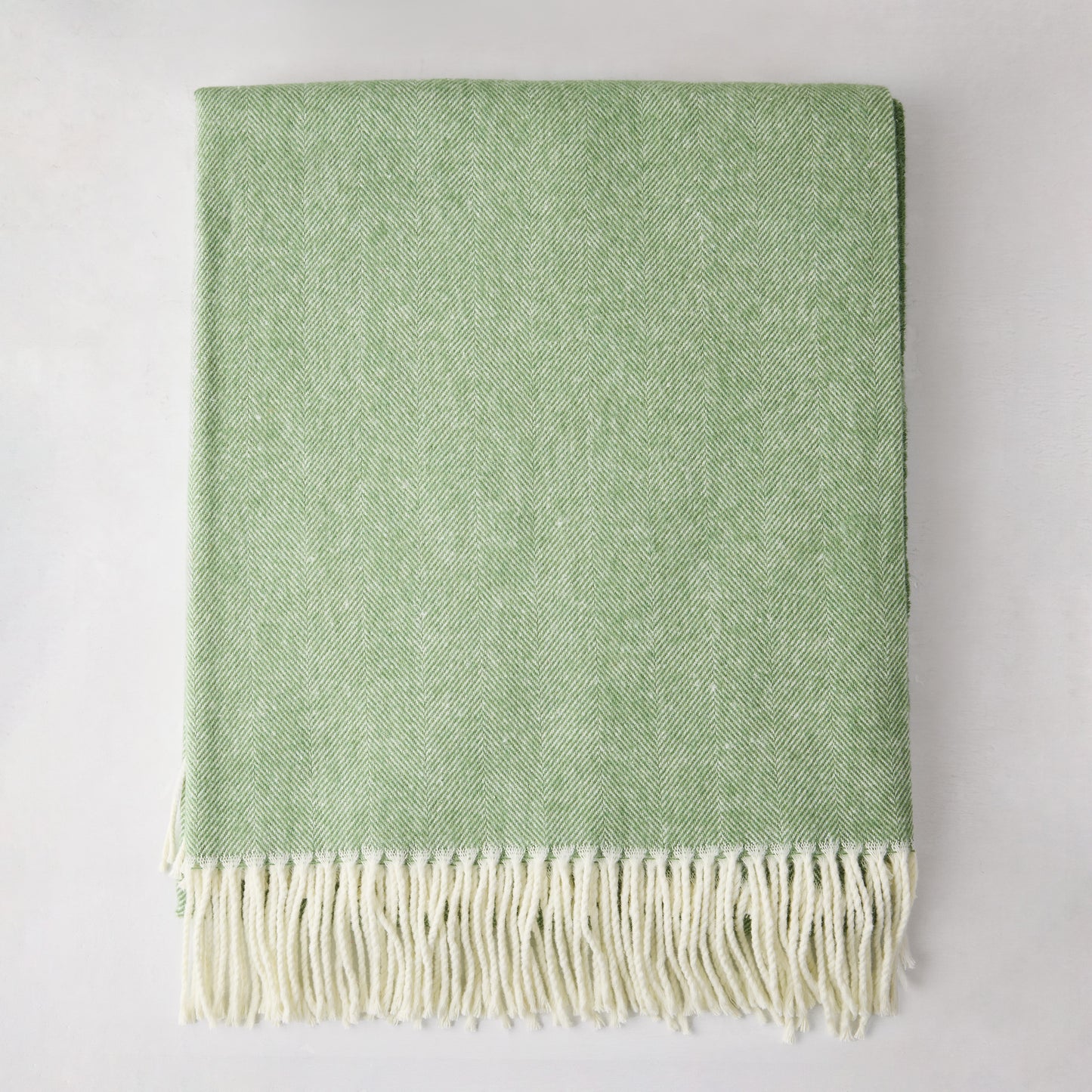 Green Italian herringbone throw blanket, folded, with cream fringe.