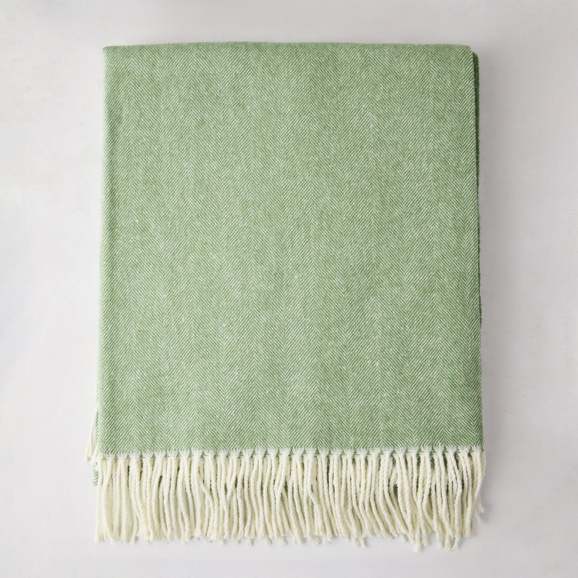 Green Italian herringbone throw blanket, folded, with cream fringe.