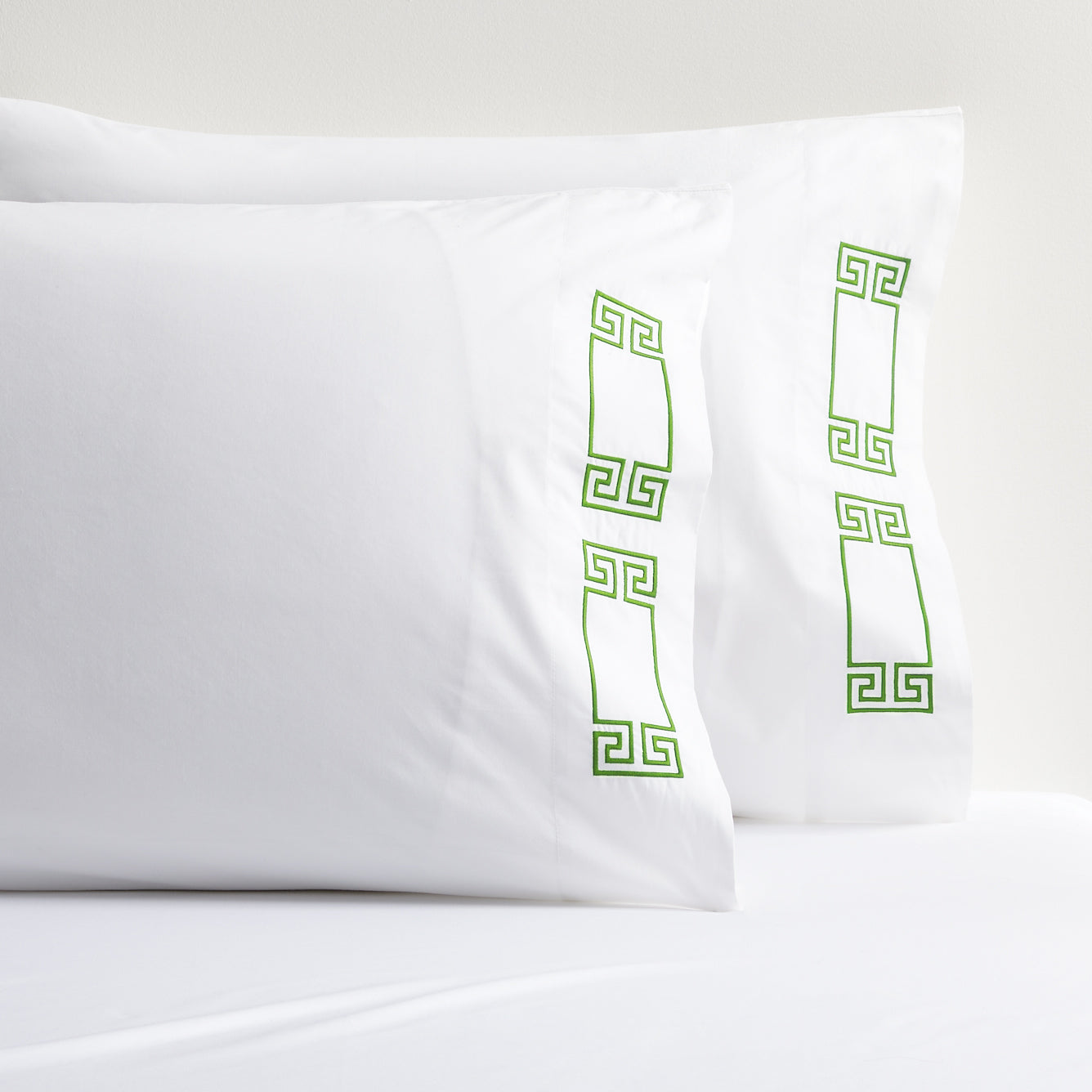 White percale pillow shams with green embroidered Greek key border.