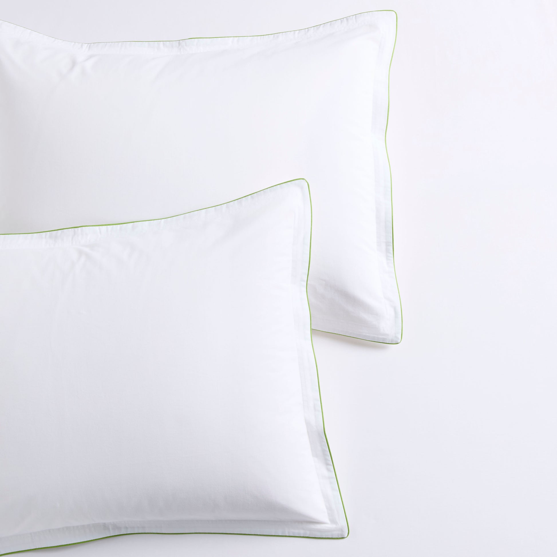 White percale duvet shams with delicate green piping and subtle double-stitch detailing.