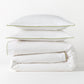 White percale duvet and two shams with green piping, stacked neatly.