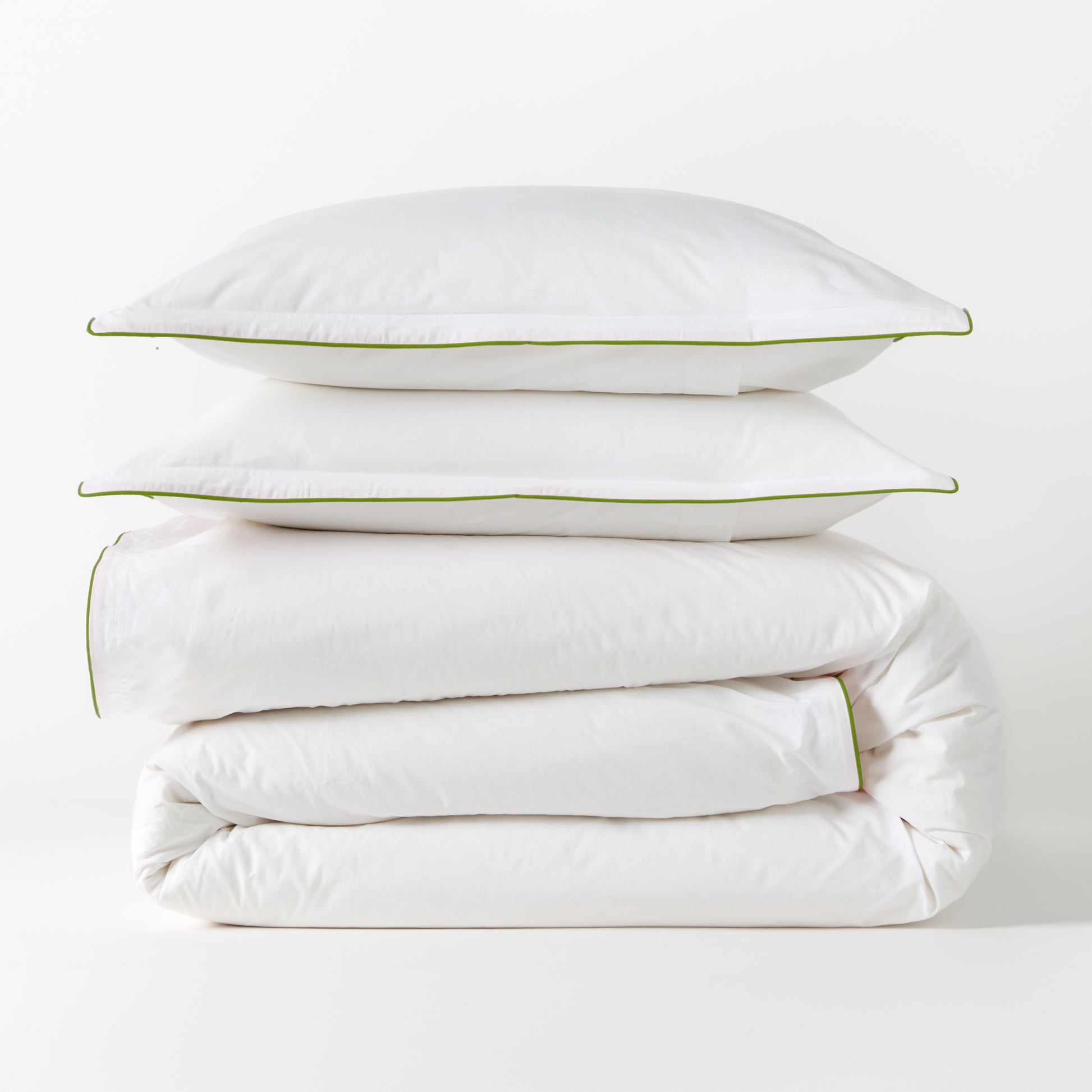 White percale duvet and two shams with green piping, stacked neatly.