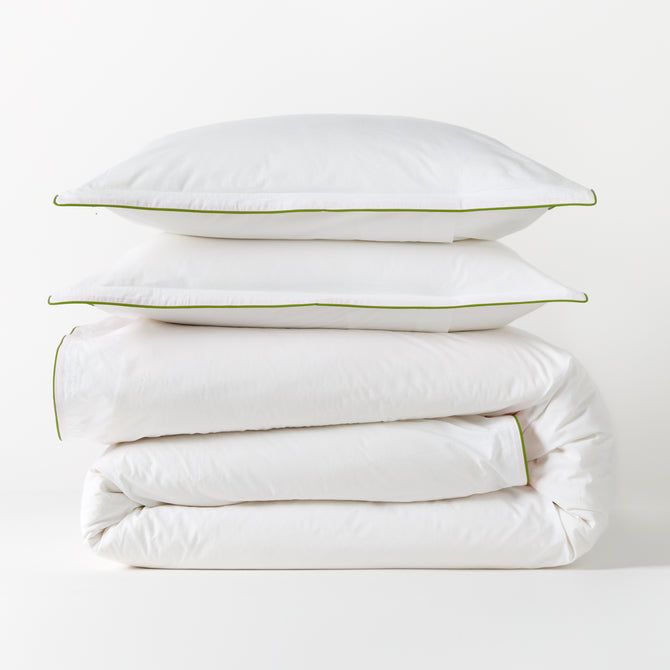White percale duvet and two shams with green piping, stacked neatly.