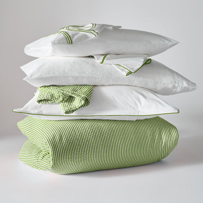 Stacked green seersucker stripe organic cotton duvet and shams with white sheets featuring green piping.