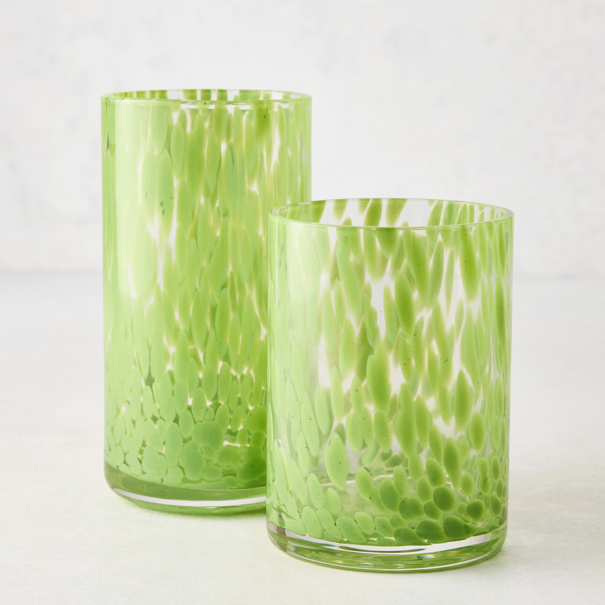 Two clear glass highball glasses with bright green spotted patterns, one tall and one shorter.
