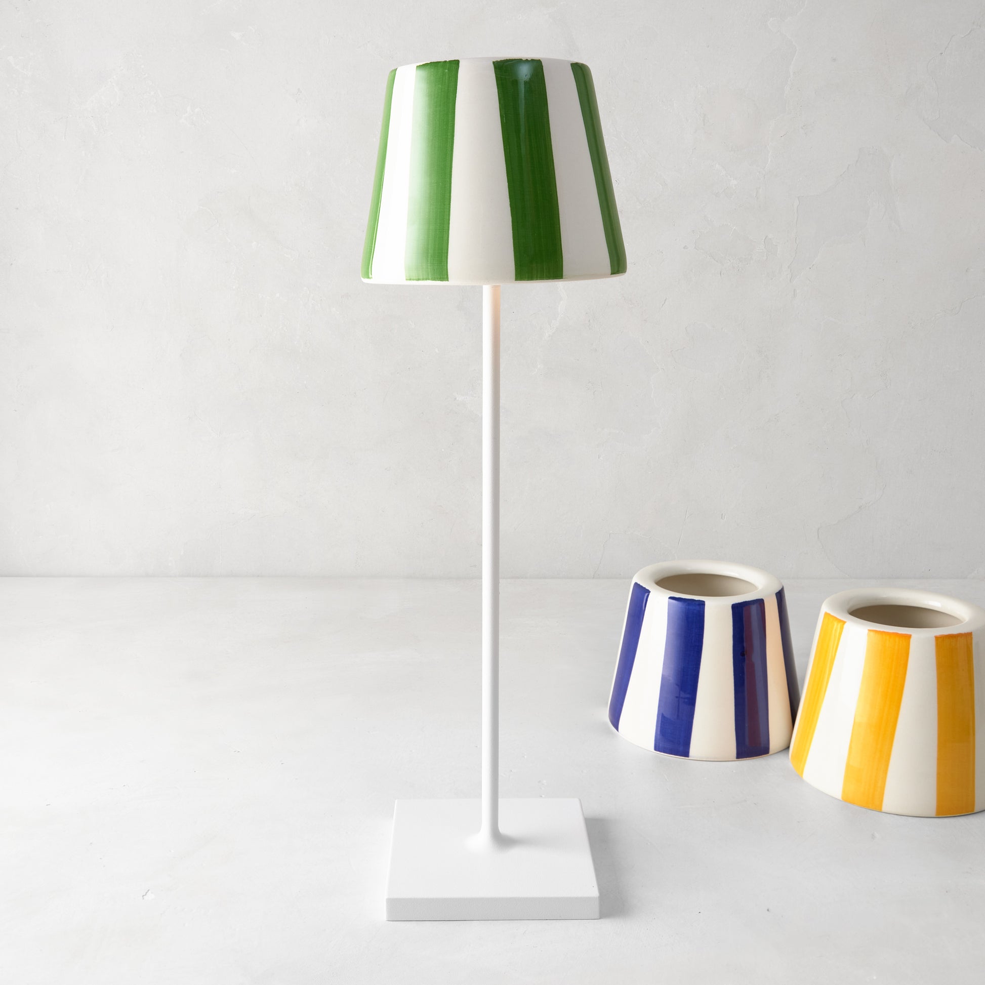 Green and white striped ceramic lamp shade on a white lamp, with blue and yellow striped shades nearby.