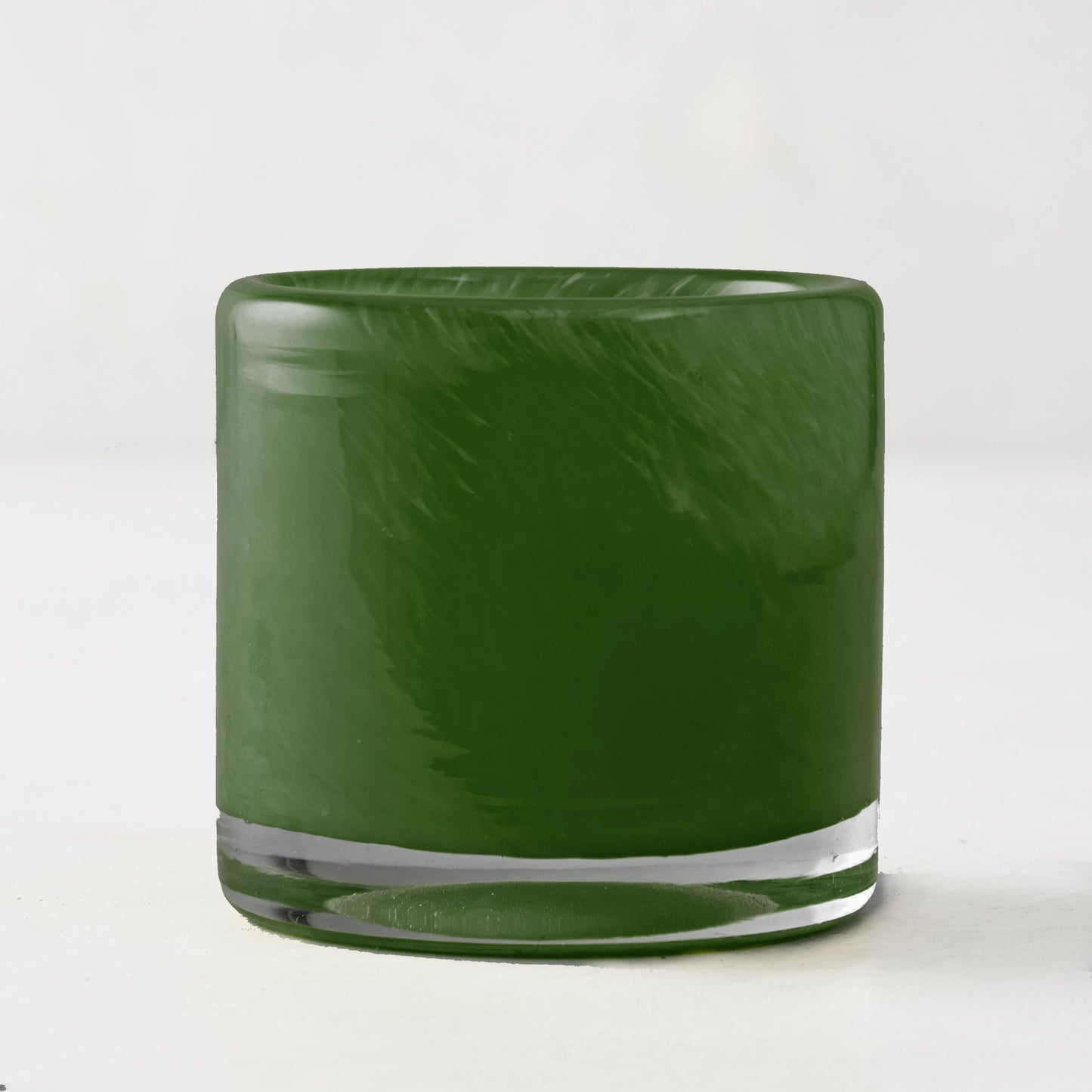 Mouth-blown, hand-formed green votive glass candle holder with clear base.