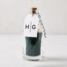 Green with white tip oversized matches in a clear glass bottle with a cork stopper and HG tag.