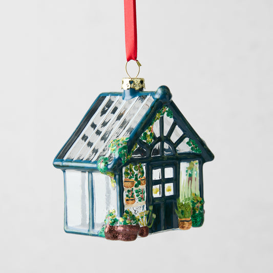 Hand-painted glass greenhouse Christmas ornament with blue frame, glittered plants, and red ribbon hanger.