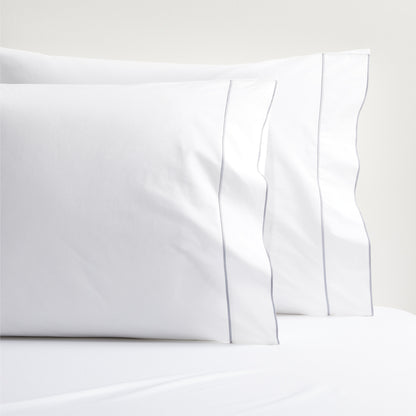 White percale pillowcases with a grey satin stitch border, stacked on a white sheet.