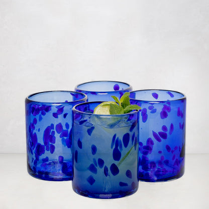Four handmade blue tortoise double old-fashioned glasses, one with a cocktail, lime, and mint.