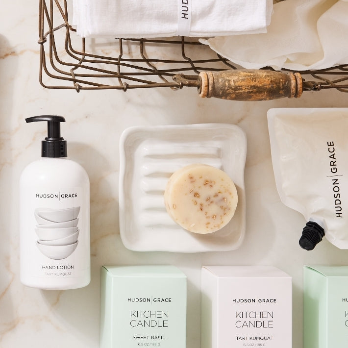 White ceramic soap dish with ridges, a bar of soap, and hand lotion on a marble surface.