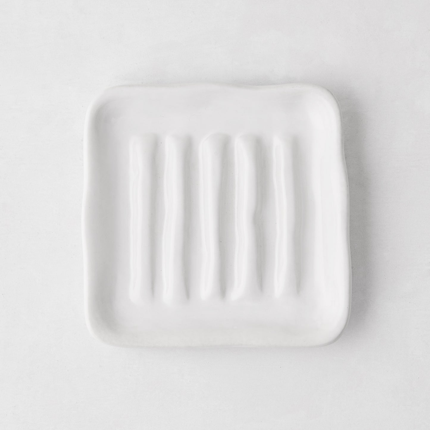 White, organic-shaped Montes Doggett ceramic soap dish with multiple ridges, 5" square.