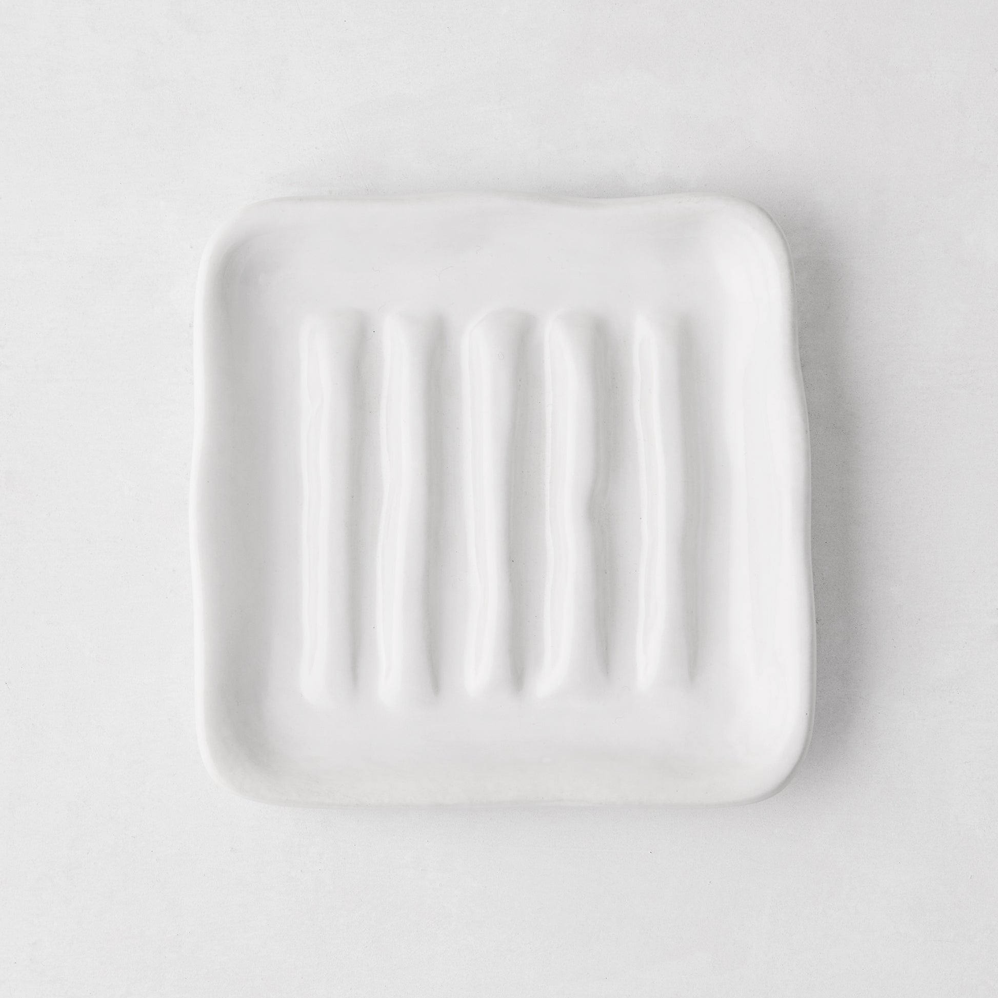 White, organic-shaped Montes Doggett ceramic soap dish with multiple ridges, 5" square.