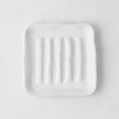 White, organic-shaped Montes Doggett ceramic soap dish with multiple ridges, 5" square.