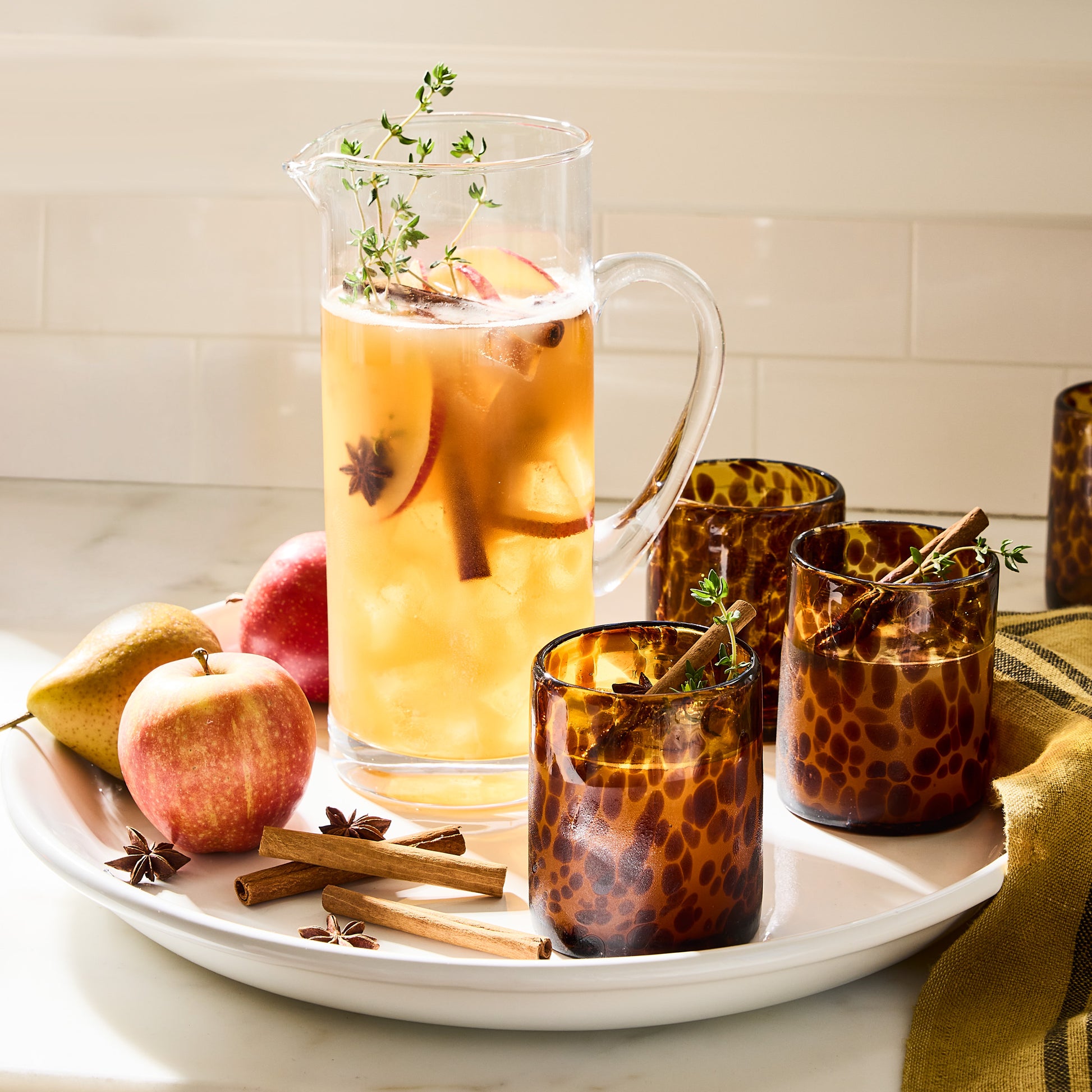 Handmade 12 oz. tortoise double old-fashioned glasses with a pitcher of cider, apples, pears, and spices.