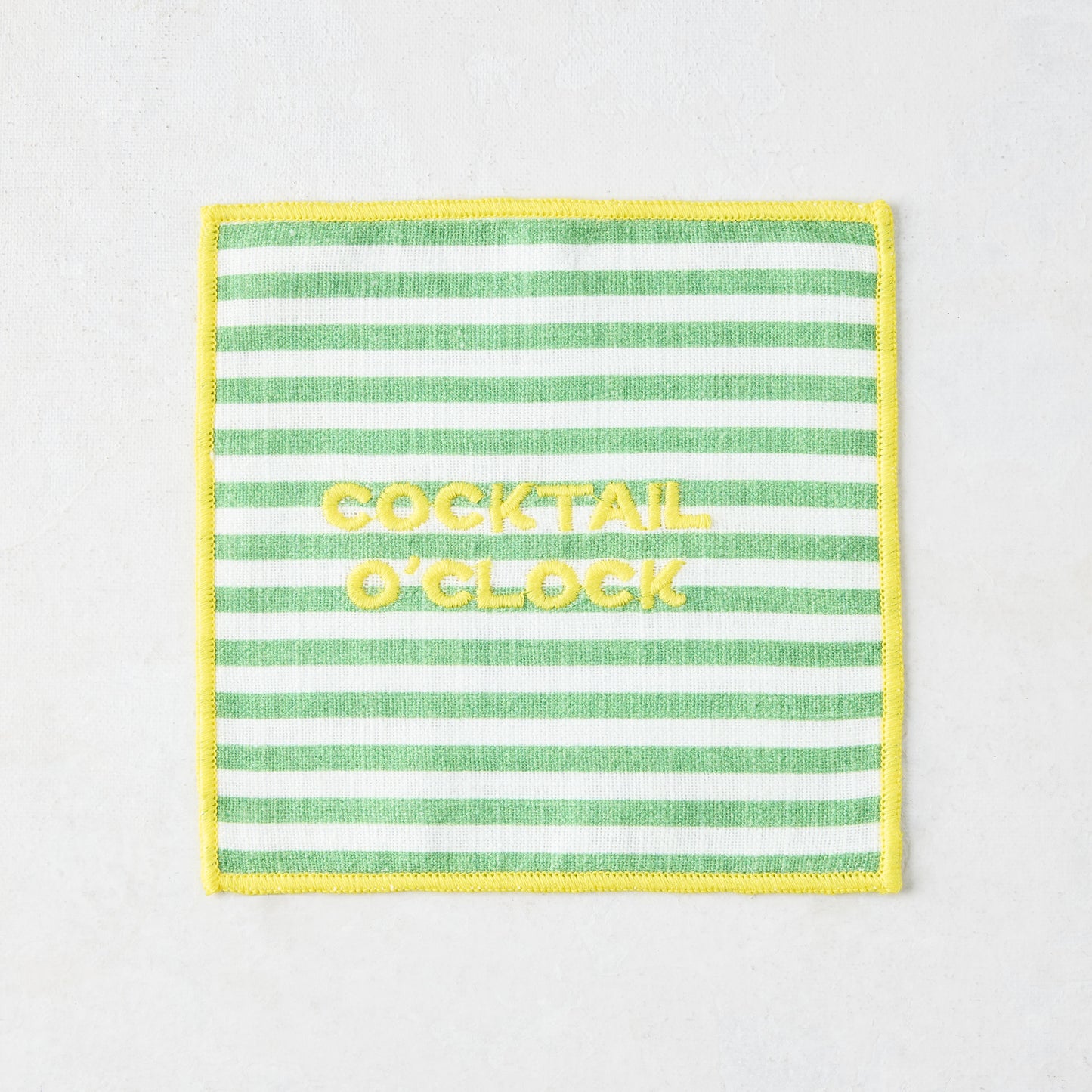 Green and white striped cotton coaster with yellow "COCKTAIL O'CLOCK" embroidery and yellow border.
