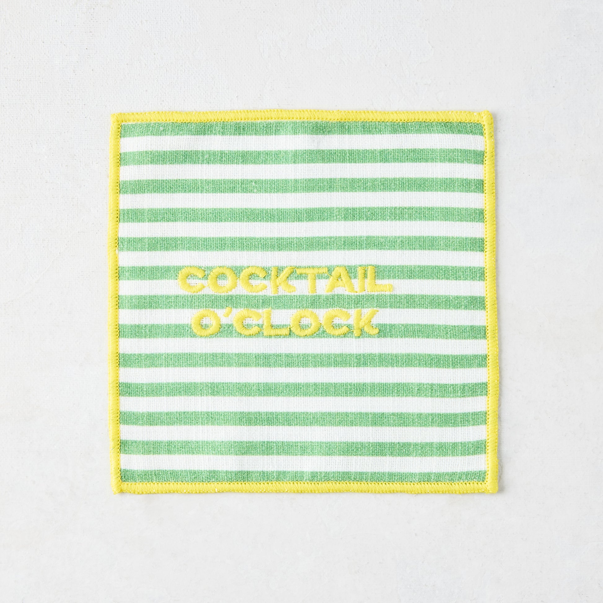 Green and white striped cotton coaster with yellow "COCKTAIL O'CLOCK" embroidery and yellow border.