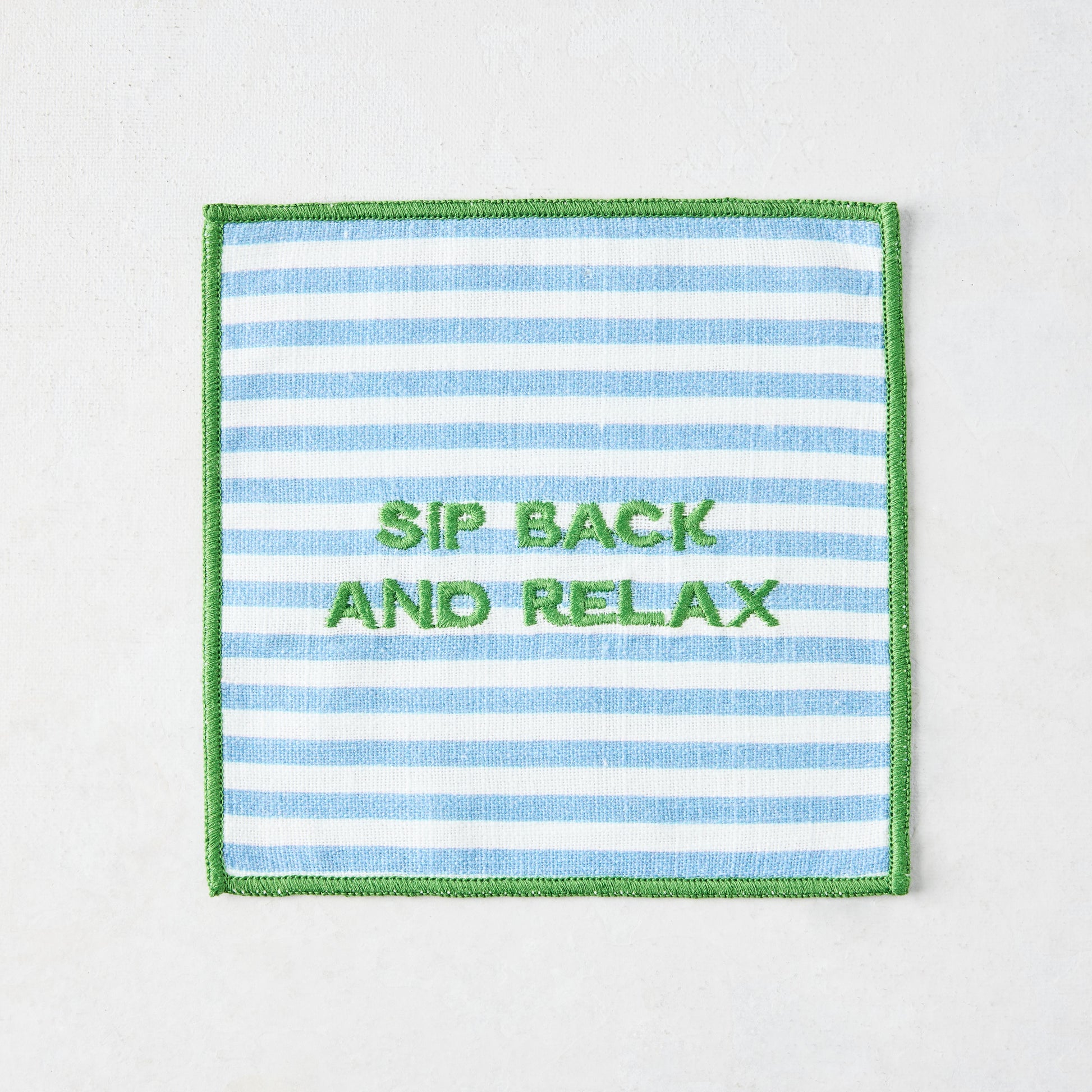 Blue and white striped cotton coaster with green embroidered "SIP BACK AND RELAX" text and green border.