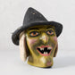 Vintage-style papier-mâché witch candy bucket with a distressed green face, black hat, and snaggletooth grin.