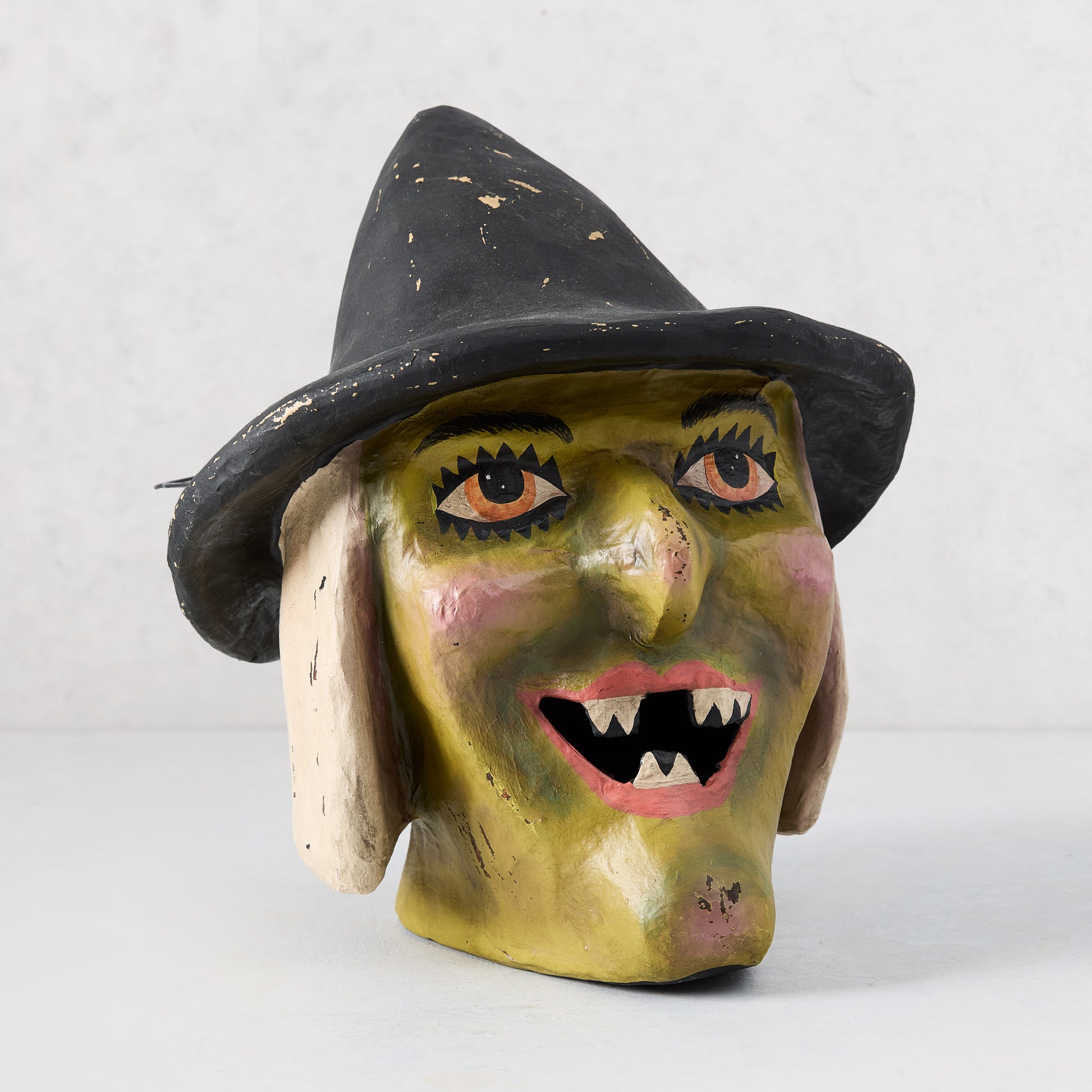 Vintage-style papier-mâché witch candy bucket with a distressed green face, black hat, and snaggletooth grin.