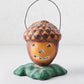 Distressed papier-mâché acorn Halloween candy bucket with a jack-o'-lantern face, green leaf base, and wire handle.