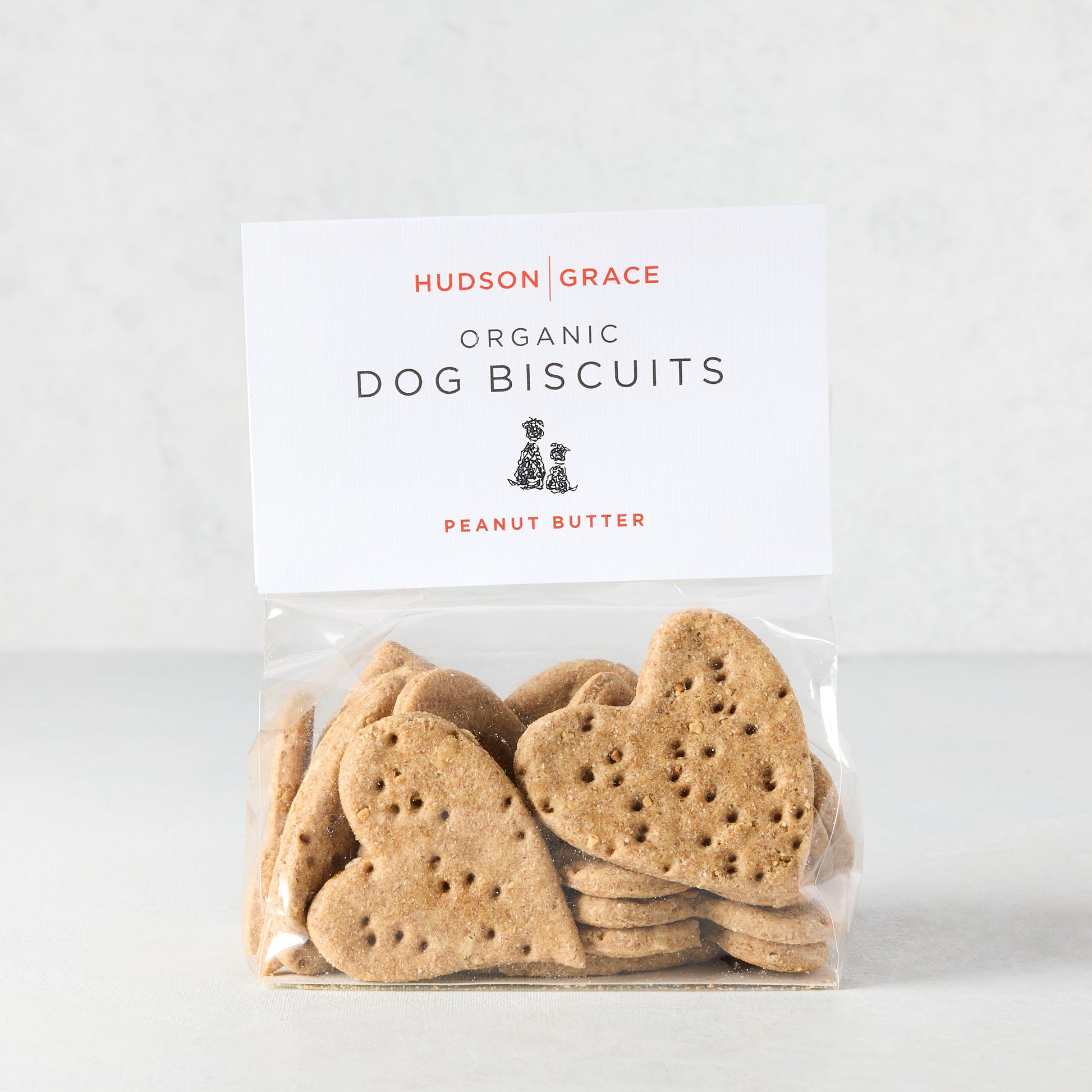 Heart-shaped peanut butter dog biscuits in a clear bag with a white "Hudson Grace Organic Dog Biscuits" label.