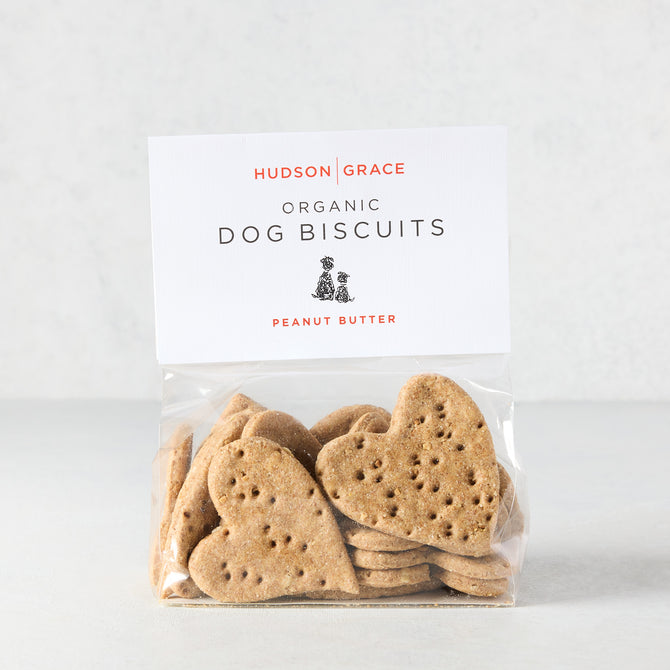 Heart-shaped peanut butter dog biscuits in a clear bag with a white "Hudson Grace Organic Dog Biscuits" label.