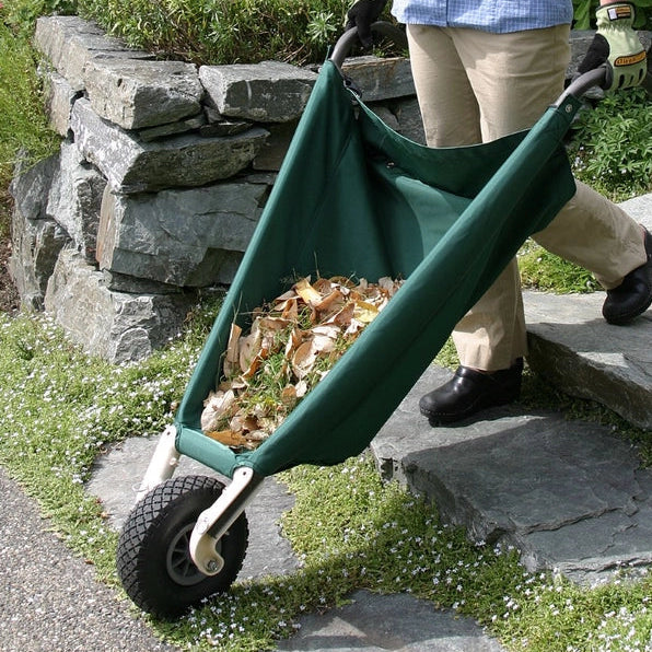 Hudson Grace green collapsible wheelbarrow being used to transport garden debris on a stone path.