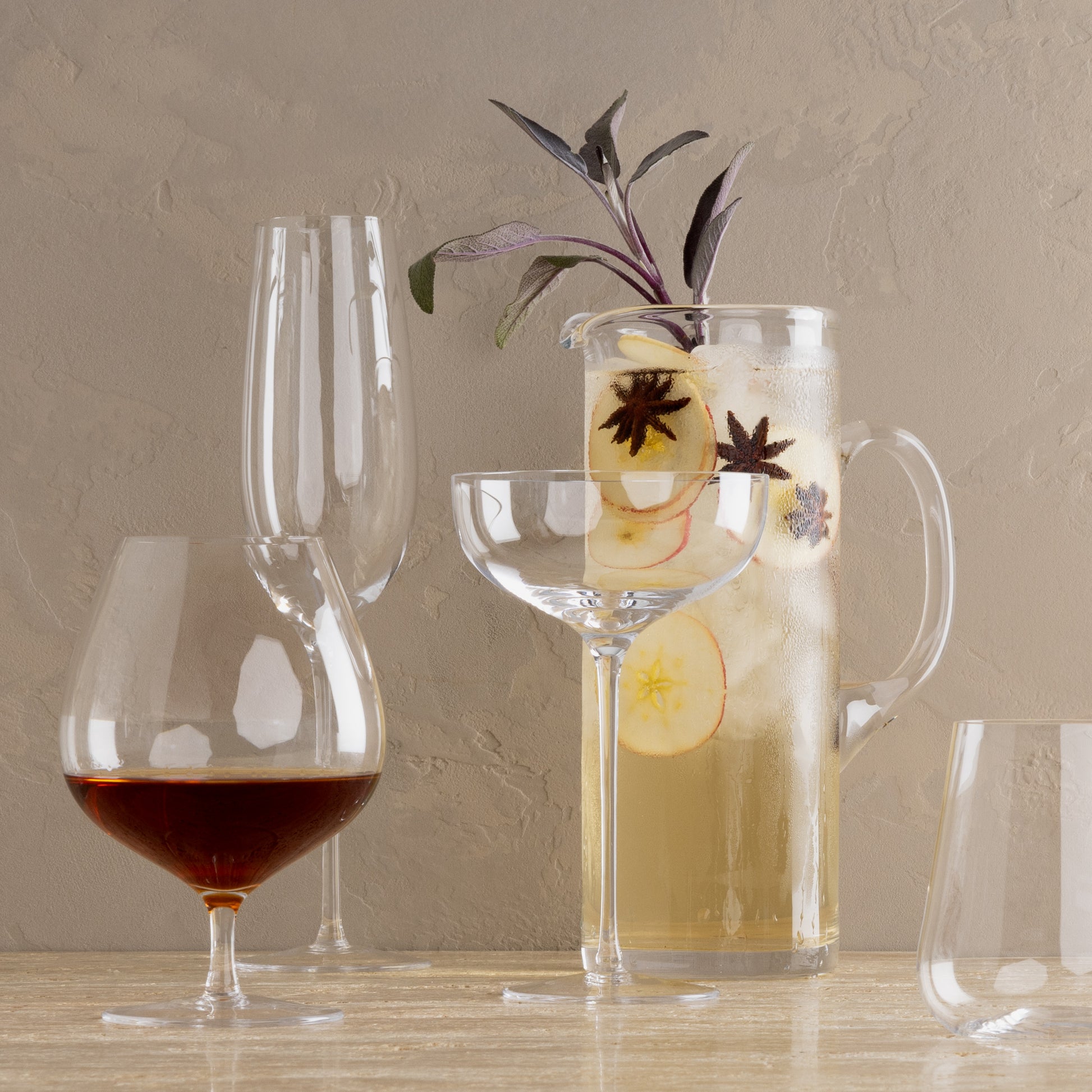 Clear, mouth-blown HG Heritage Champagne Glass, coupe, and snifter with a pitcher of apple cider.