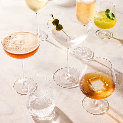 HG Heritage Cognac Glass with amber liquid and ice cube, surrounded by other drinkware.