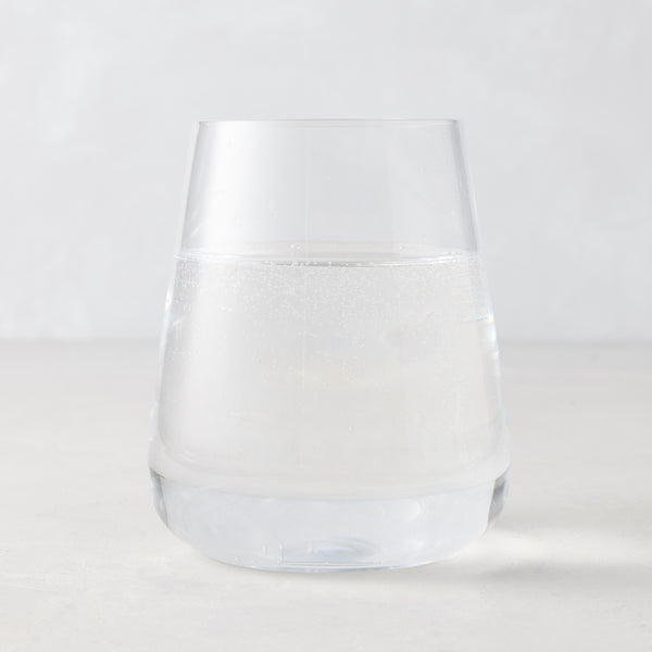 Clear HG Heritage Stemless Glass, mouth-blown, filled with water, on a light background.