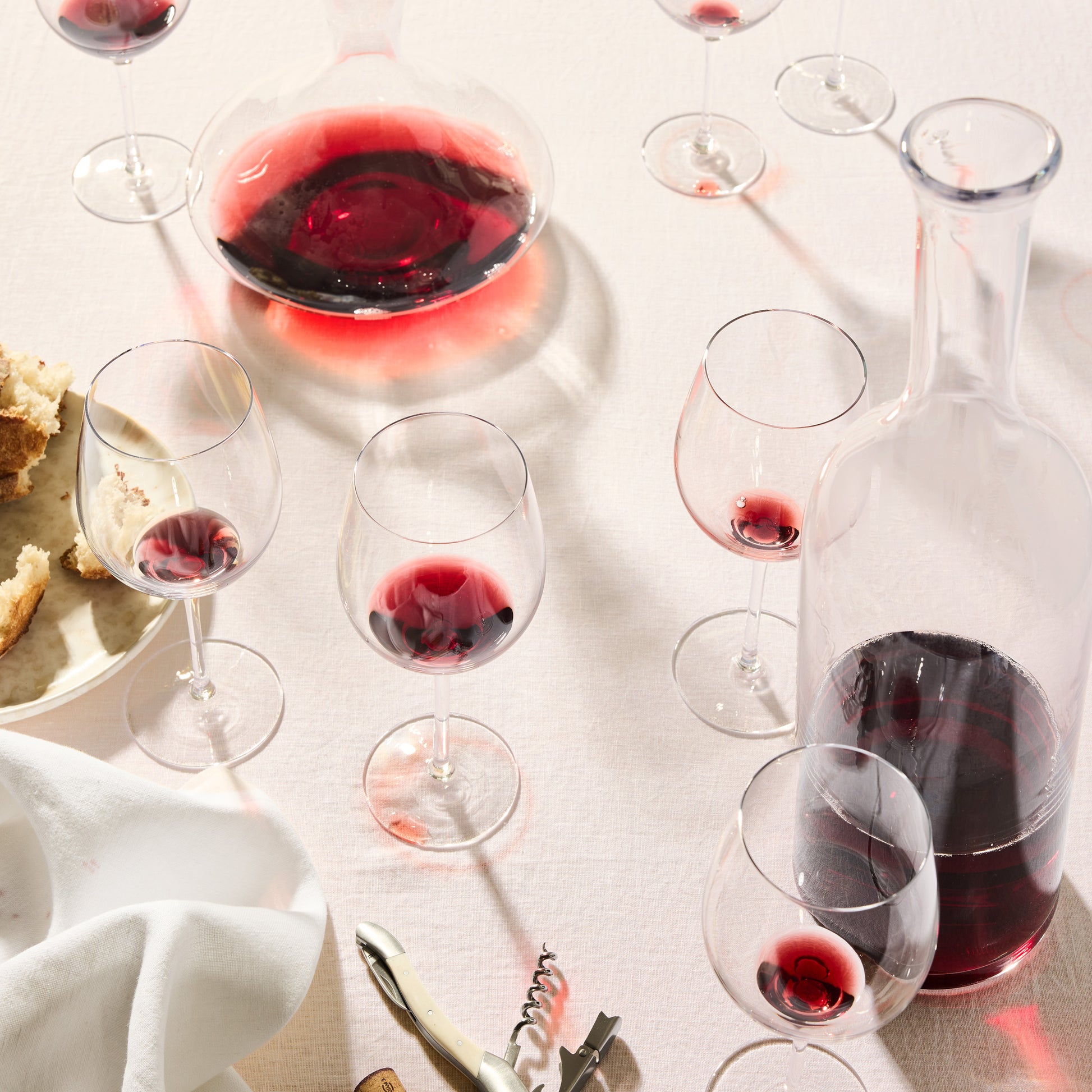 Clear mouth-blown HG Heritage wine glasses and decanters with red wine on a light tablecloth.