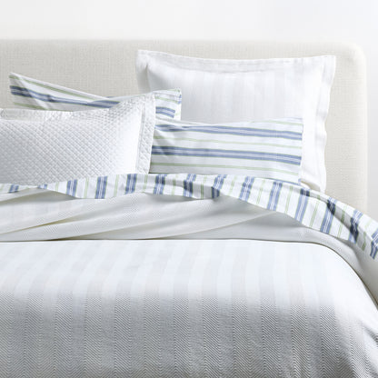 White Queen Herringbone Matelassé Coverlet with striped and quilted shams on a bed.