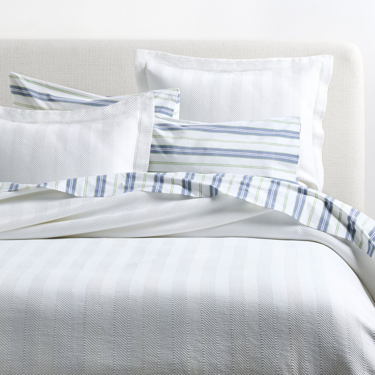 White Herringbone Matelassé Pillow Shams, 100% cotton, with subtle texture and a striped accent pillow.