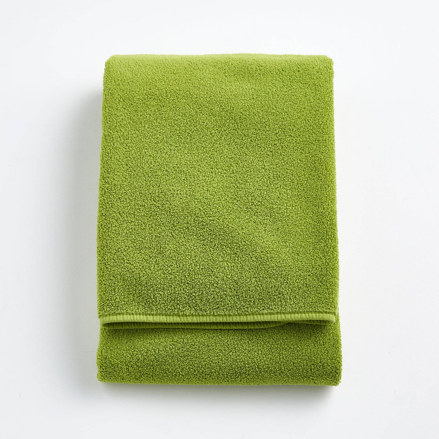 Folded aloe green Signature bath towel made of soft zero-twist cotton with bias piping detail.