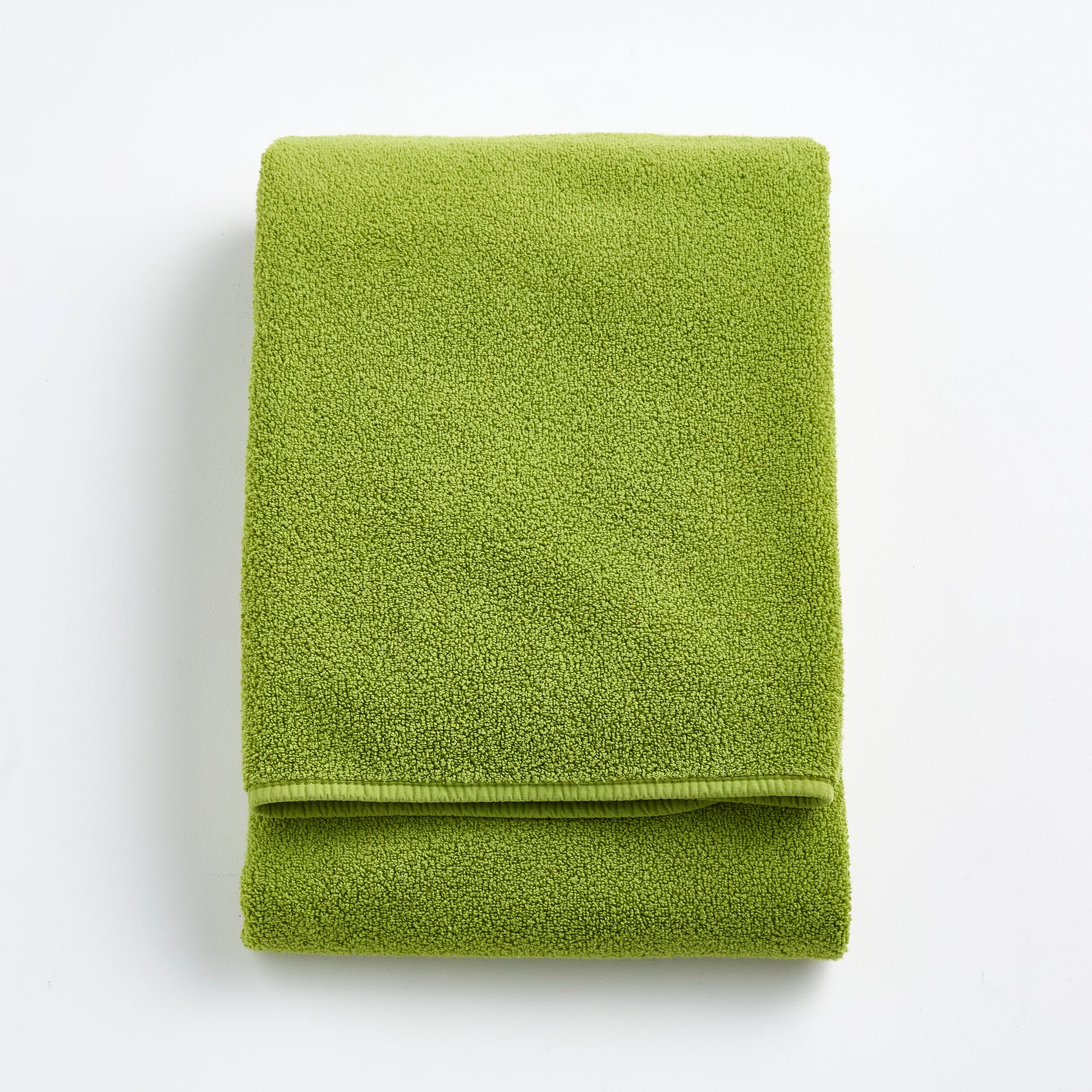 Folded aloe green Signature bath towel made of soft zero-twist cotton with bias piping detail.