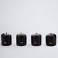 Four black unscented 2" votive candles with gold HG logo, made from paraffin and amber tree resin.